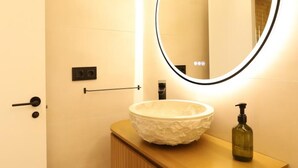 A bathroom with a round mirror, a white basin, a wooden countertop, a soap dispenser, and a towel rack. - Modern apartment 5 min from the beach (Puerto de Sagunto)