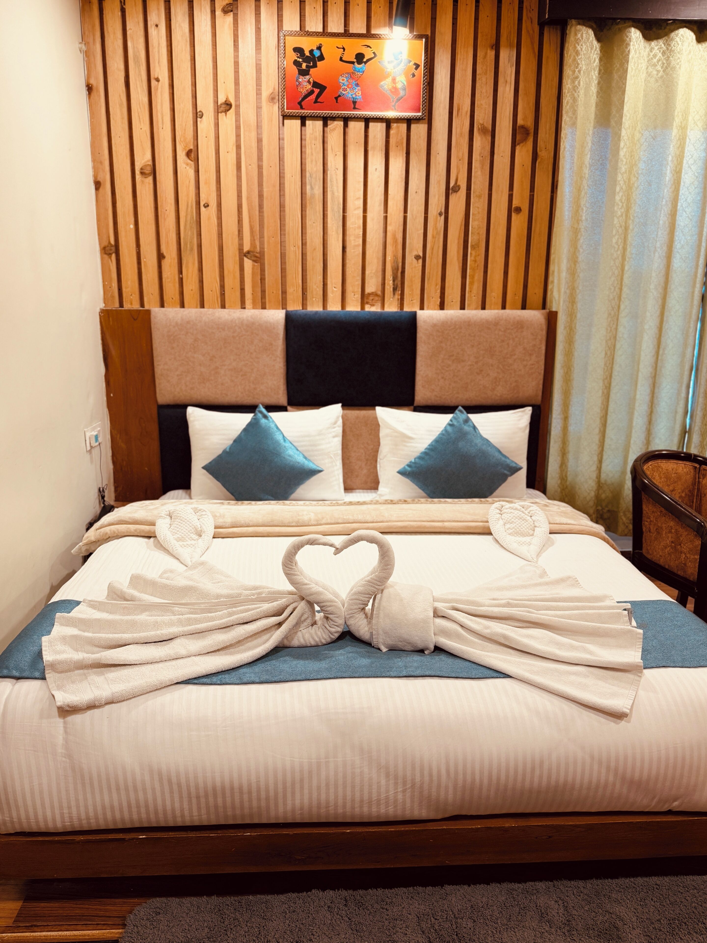 A neatly made bed with towels arranged in a heart shape, a wooden headboard, and a framed picture on the wall.