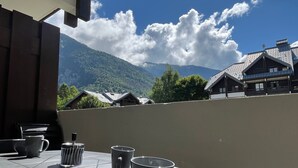 A balcony with a table, two cups, and a container. In the background, there are mountains and houses. - Renovated studio in village center with balcony (Samoëns)