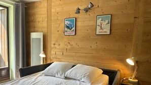 A wooden-paneled room with a bed, two wall-mounted lamps, and two framed posters. - Renovated studio in village center with balcony (Samoëns)