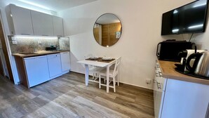 A compact kitchen with a dining area, a round mirror, and a flat-screen TV. - Renovated studio in village center with balcony (Samoëns)