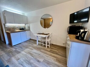 A compact kitchen with a dining area, a round mirror, and a flat-screen TV.