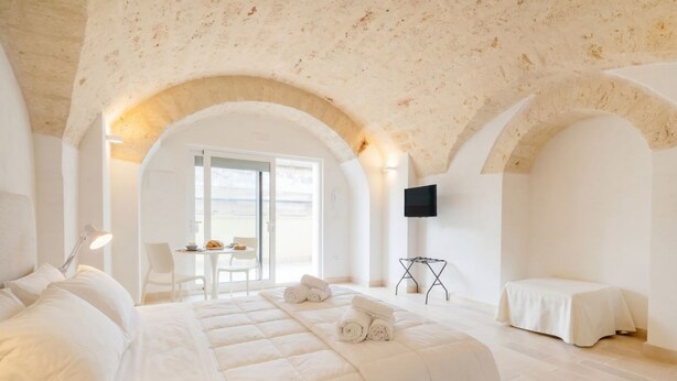 Habitación de hotel con una cama grande, televisión, una mesita y techo abovedado.