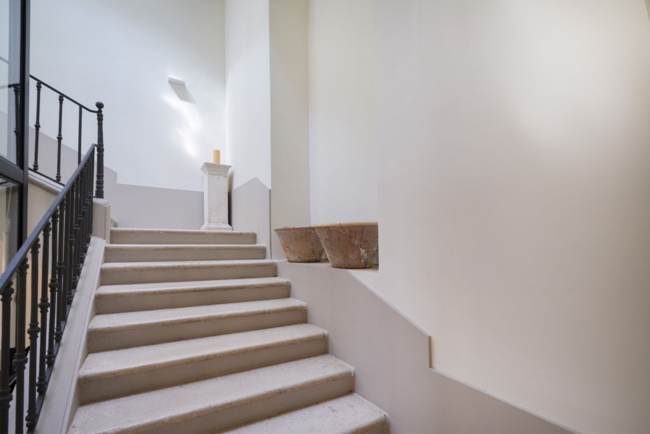 Eine Treppe mit schwarzer Geländer, weißen Wänden und einem kleinen weißen Podest oben.