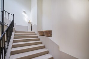 A staircase with a black railing, white walls, and a small white pedestal at the top.