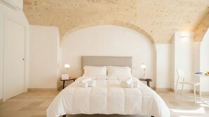 Un dormitorio con una cama grande, dos mesitas de noche con lámparas, una silla blanca y un techo de piedra.