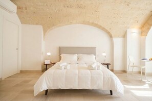 Une chambre à coucher avec un grand lit, deux tables de chevet avec des lampes, une chaise blanche et un plafond en pierre.