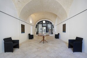 Un hall d’entrée spacieux avec un haut plafond en arc de cercle, une table ronde centrale et des chaises recouvertes de tissu noir.