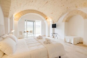 Une chambre d’hôtel avec un grand lit, une télévision, une petite table et un plafond en arc de cercle.
