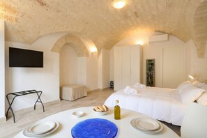A bedroom with a bed, a table with plates, a bottle, and a TV on the wall. - Palazzo della Torre 002 - Historical modern stay (Bari)