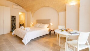 Un dormitorio con una cama, mesitas de noche, una pequeña mesa de comedor y una silla blanca.