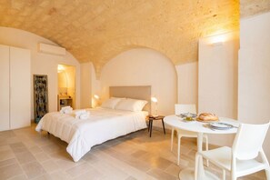 Une chambre à coucher avec un lit, des tables de chevet, une petite table à manger et une chaise blanche.