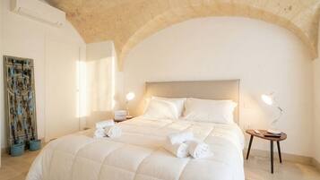 A hotel room with a large bed, a headboard, a bedside table with a lamp, and a wall-mounted air conditioner.