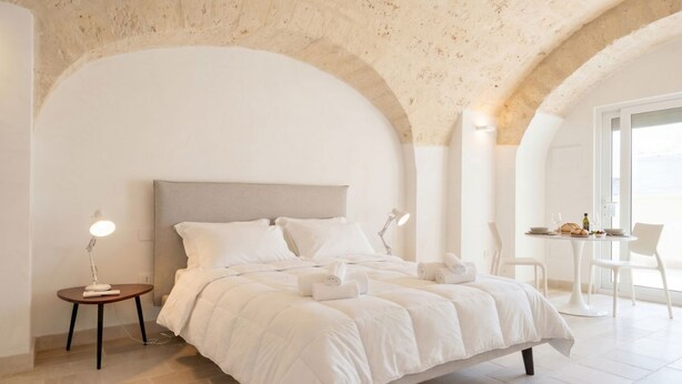 Un dormitorio con una cama, una mesita de noche con lámpara, y un área de comedor con sillas y una mesa.