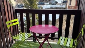 A balcony with a round table and two chairs, a wooden fence, and a view of parked cars and buildings in the background. - Cozy studio 5 pers. at the slopes (Saint-François-Longchamp)