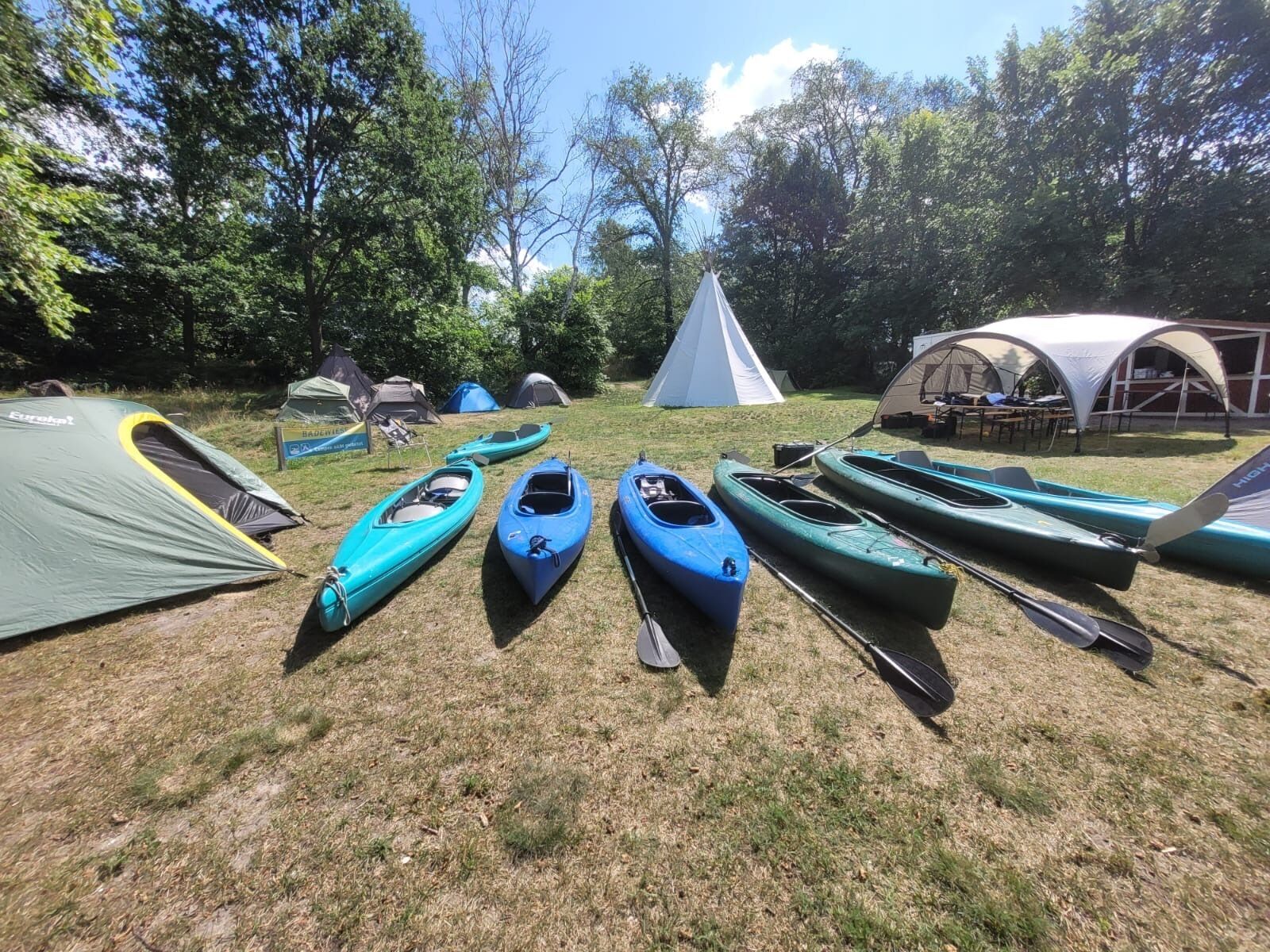 Un terrain de camping avec plusieurs tentes et des kayaks alignés sur l’herbe.