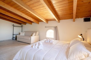Ein Schlafzimmer mit Holzboden, einem Bett mit weißer Bettwäsche, einer Couch, einem Fenster mit Vorhängen und einer Lampe.