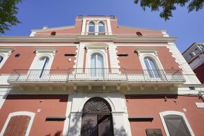 A red building with a central entrance, two windows on each side, and a balcony with railings.