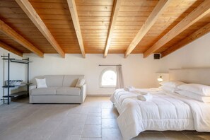 A bedroom with a wooden ceiling, a bed, a sofa, a window, and a wall-mounted shelf.