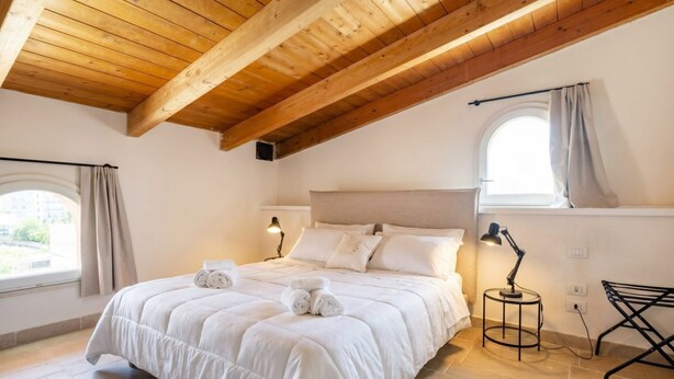 A bedroom with a wooden ceiling, a bed with white bedding, two bedside lamps, and a window with curtains.