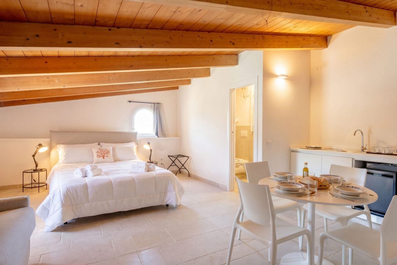Una camera da letto con un letto, lampade sui comodini, un piccolo tavolo e vista sulla cucina.