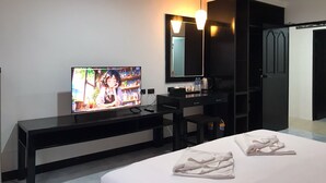Una habitación de hotel moderna con una televisión de pantalla plana sobre una mesa consola negra, una cama con toallas blancas ordenadas, un escritorio negro con una silla y un espejo grande sobre el mueble de espejo.