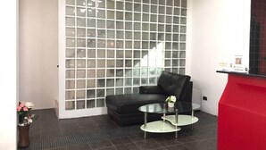 Una habitación moderna con un separador de vidrio, un sofá de cuero negro, una mesa de centro de vidrio y un mostrador de recepción rojo.