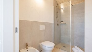 Un baño moderno con ducha de mampara de vidrio, inodoro blanco y bidé.