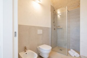A modern bathroom with a glass-enclosed shower, a white toilet, and a bidet.