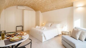 Un dormitorio con cama, un sofá, una mesa con platos y una botella, y una silla.