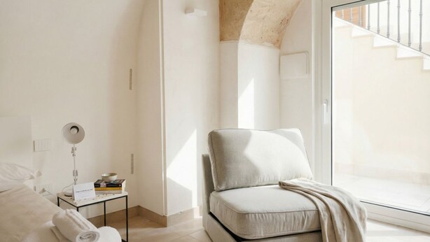 Une chambre moderne avec un lit, une table de chevet avec une lampe, un canapé et une grande fenêtre donnant sur un escalier.