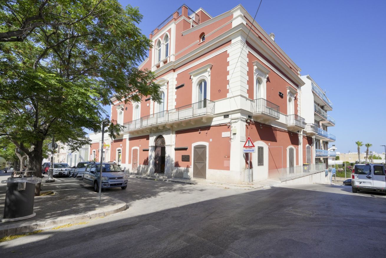 Un edificio a due piani con facciata rosso e bianco, un balcone al secondo piano e un ingresso con cancello.