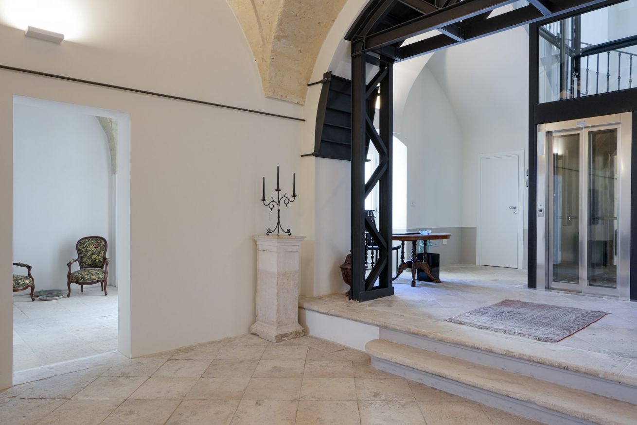 Ein geräumiger Innenraum mit hoher Decke, einer Treppe zu einem Balkon und Blick ins Freie.