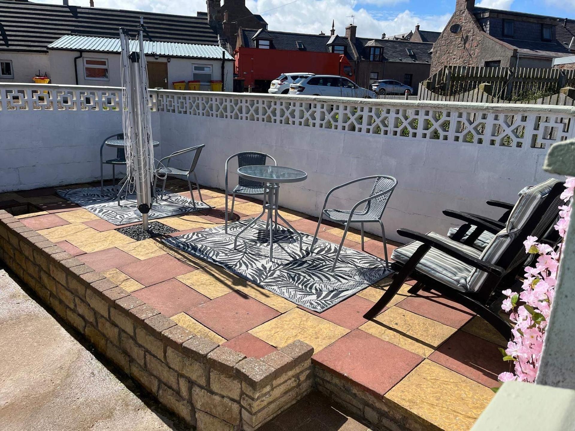 Eine Terrasse mit Ziegelmauer, einem Metalltisch, zwei Stühlen und einer Bank.