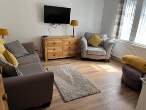 A living room with a sofa, armchair, wooden dresser, and a flat-screen TV mounted on the wall. - Costal Cottage -boddam-sleeps6- Pet Friendly (Peterhead)