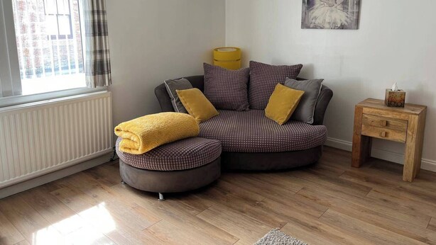 A cozy living room with a sectional sofa, a small wooden side table, and a painting on the wall. - Costal Cottage -boddam-sleeps6- Pet Friendly (Peterhead)