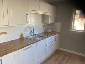 A kitchen with white cabinets, a wooden countertop, a stainless steel sink, and a kettle. - Costal Cottage -boddam-sleeps6- Pet Friendly (Peterhead)
