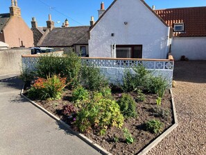 A residential property with a garden bed, a white tiled wall, and a house with a pitched roof. - Costal Cottage -boddam-sleeps6- Pet Friendly (Peterhead)