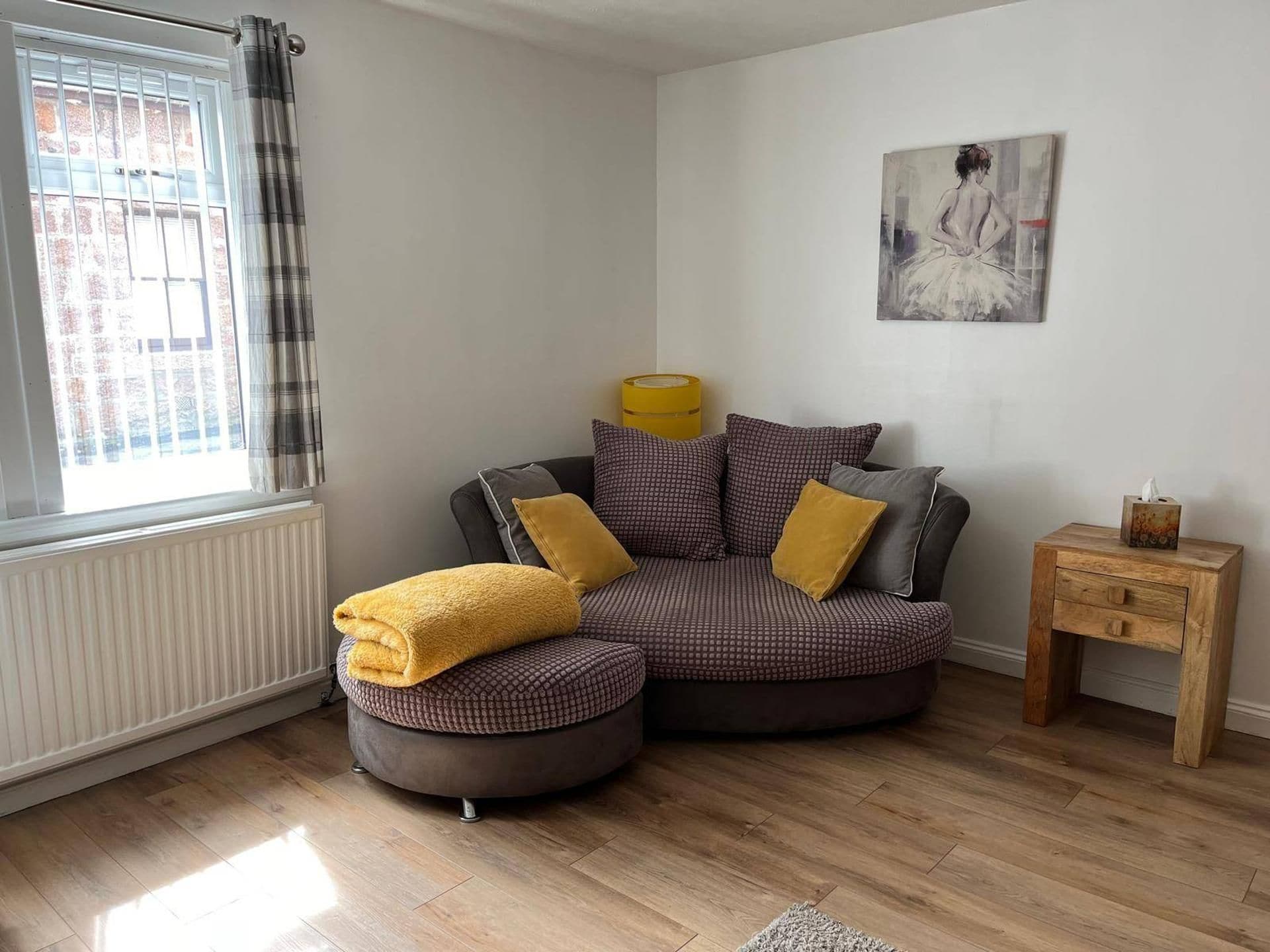 A modern living room with a sectional sofa, a small wooden side table, and a radiator.