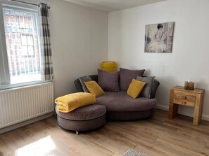 A modern living room with a sectional sofa, a small wooden side table, and a radiator. - Costal Cottage -boddam-sleeps6- Pet Friendly (Peterhead)