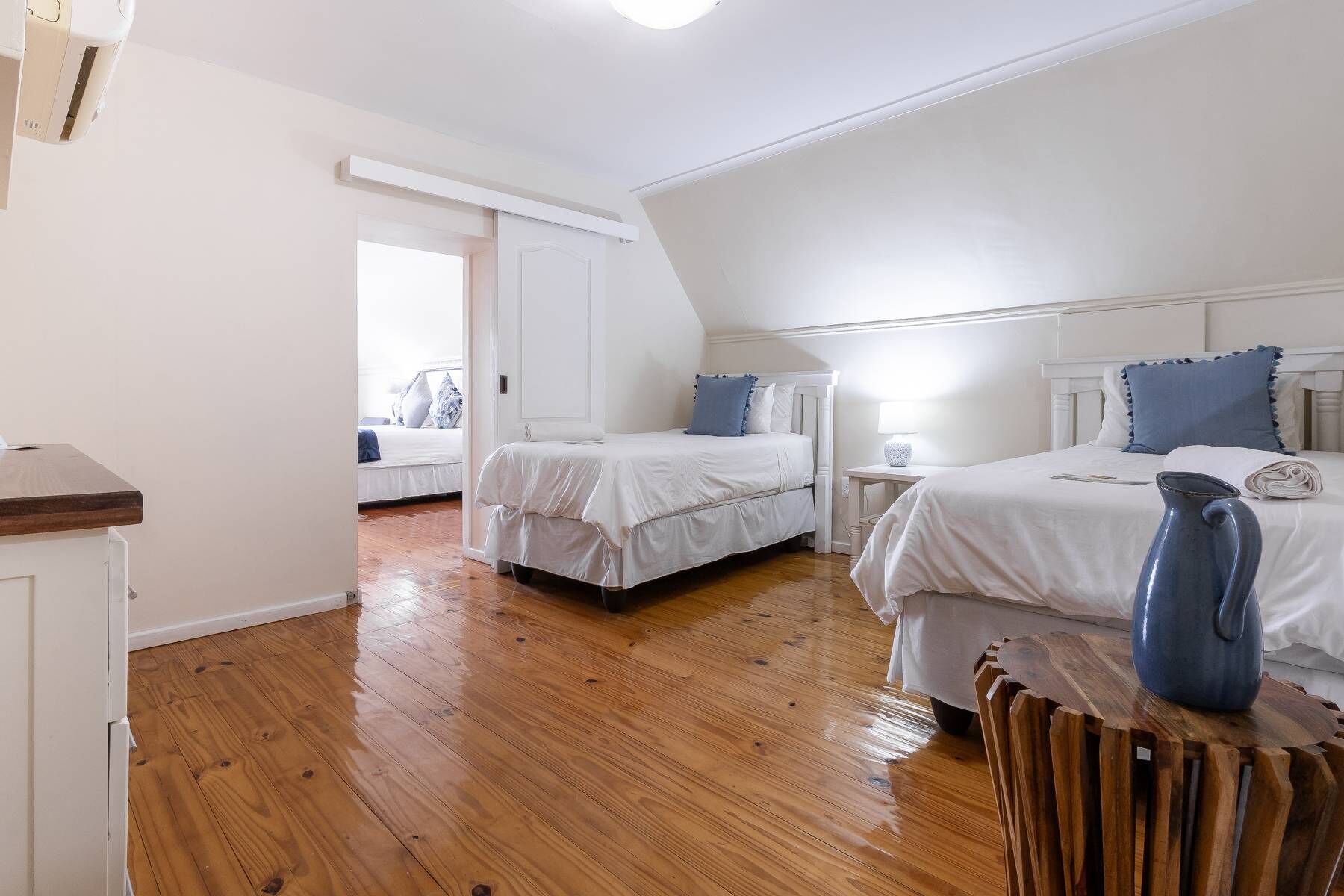 A bedroom with two beds, wooden flooring, and a white ceiling.