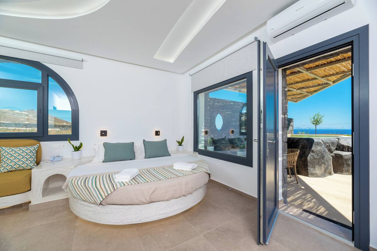 A modern bedroom with a curved bed, large windows, and a view of the sea.