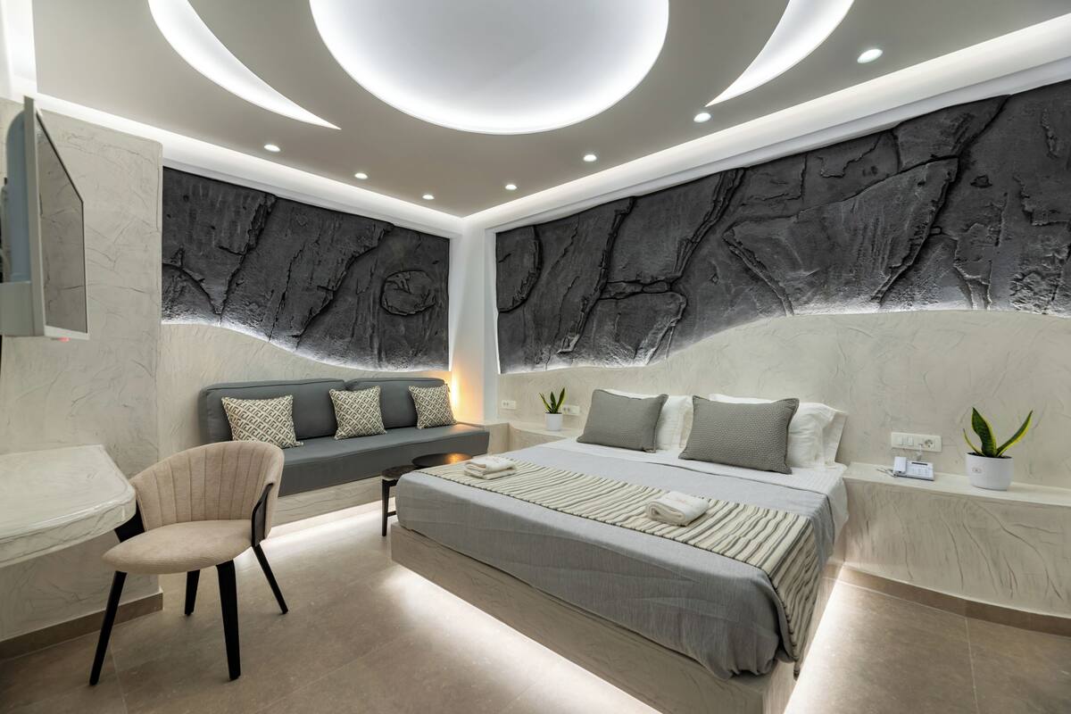 A modern bedroom with a large bed, a seating area, and a desk.
