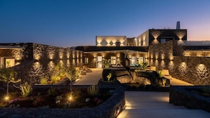 A modern building with a stone facade, a pool, and outdoor lighting. - Mperes Villas (Santorini)