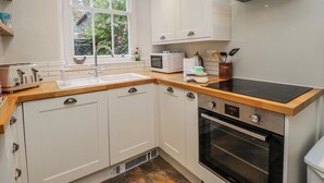 Una cocina moderna con armarios blancos, horno integrado, microondas y ventana con vistas a la vegetación.