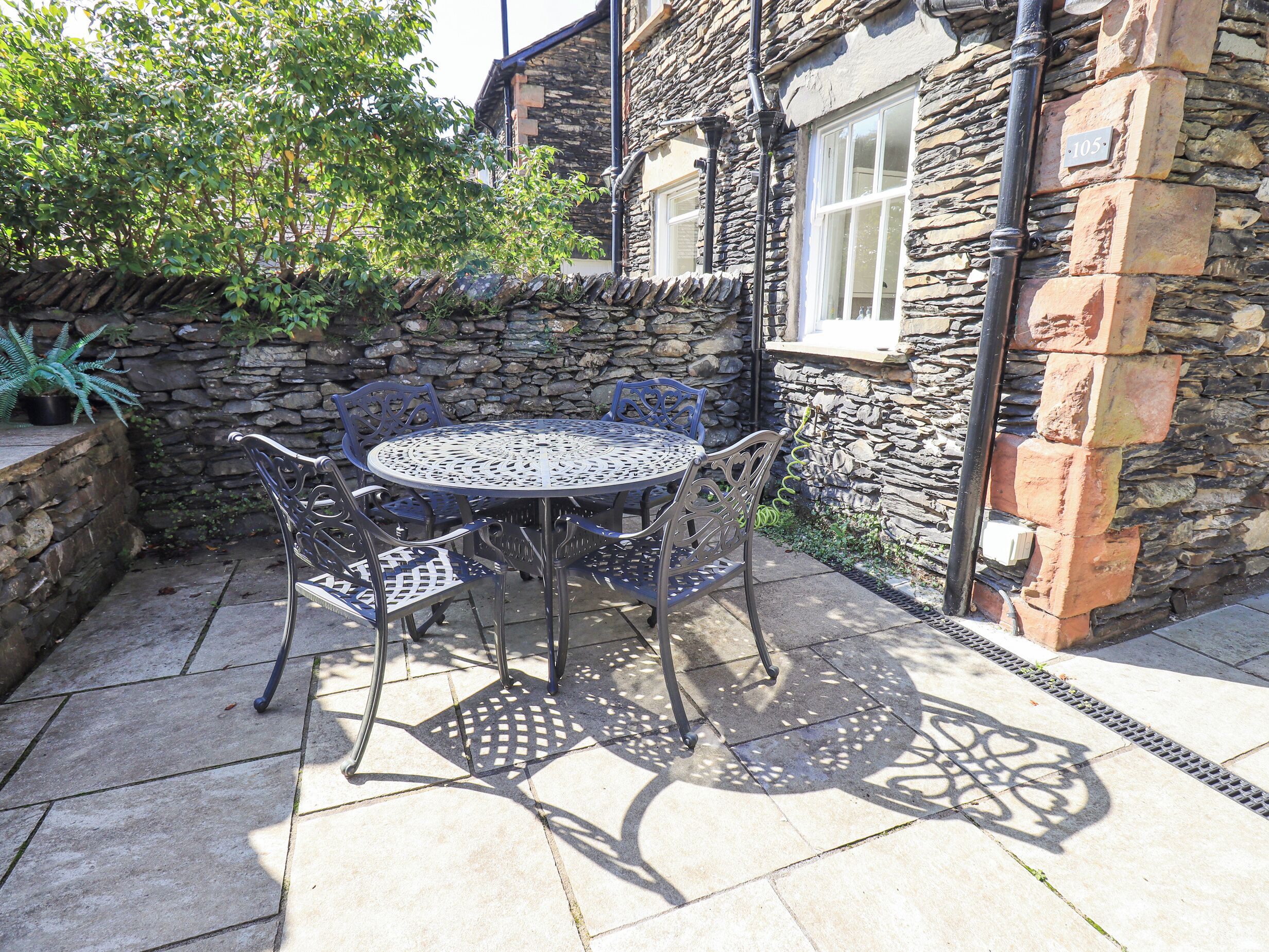 A stone building with a number plaque, a round metal table with chairs, and a stone wall with a plant.