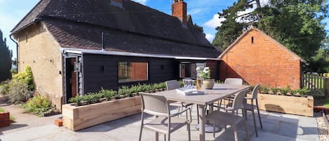 A house with a patio area featuring a table and chairs, surrounded by a garden.