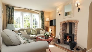 A cozy living room with a fireplace, a sofa, a coffee table, and a TV. - The Alms House East (Gloucester)
