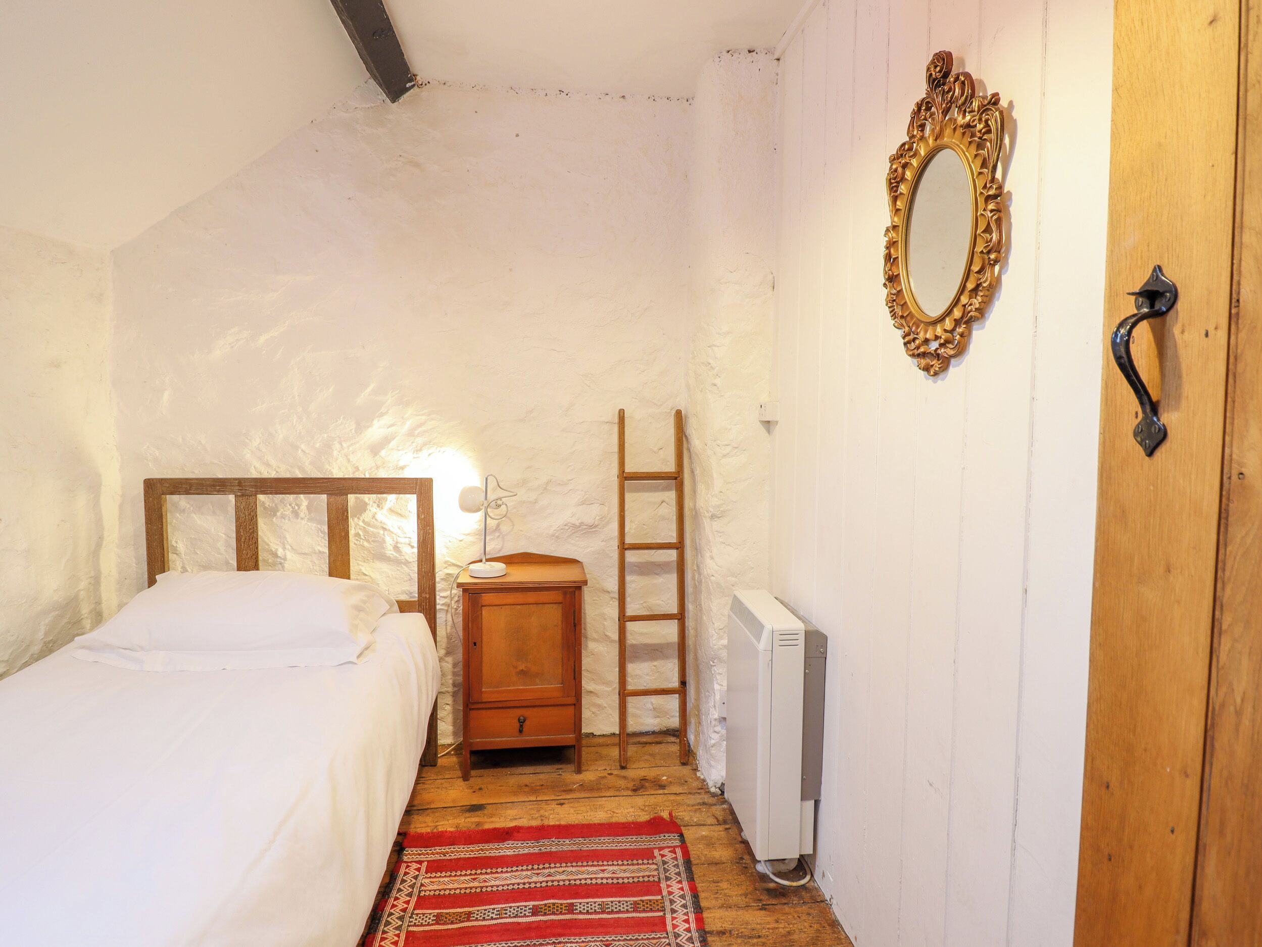Un dormitorio pequeño y acogedor con cama de madera, una mesita de noche, un radiador, una escalera y un espejo en la pared.