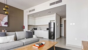 A modern living room with a grey sofa, a wooden coffee table, and a kitchen area with white cabinets and stainless steel appliances.